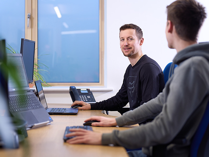 Two men at computers talking